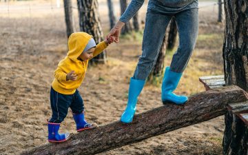 Eine Frau balanciert mit einem Kind auf einem Holzstamm